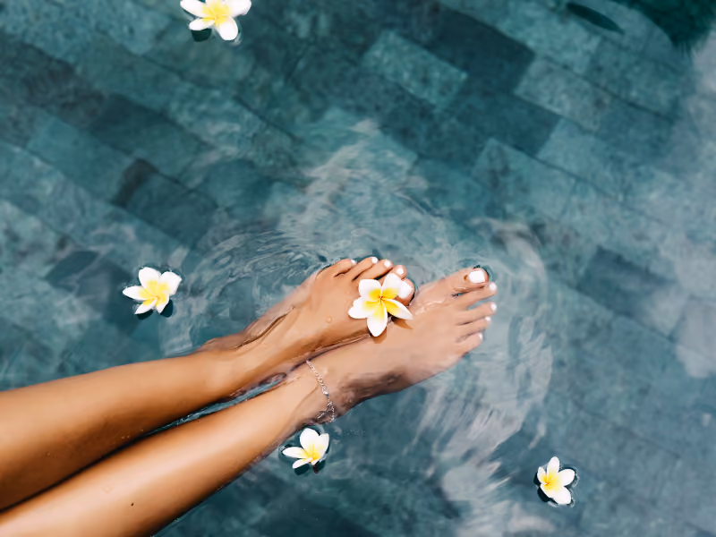 Feet cooling in a pool with frangipani flowers floating on the water